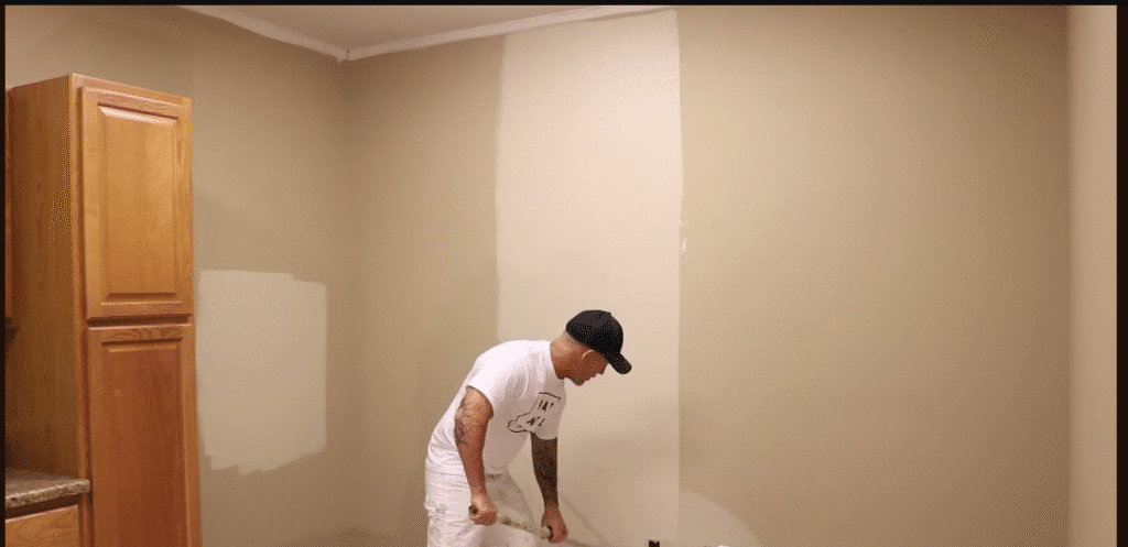 Painter rolling neutral paint on a living room wall.